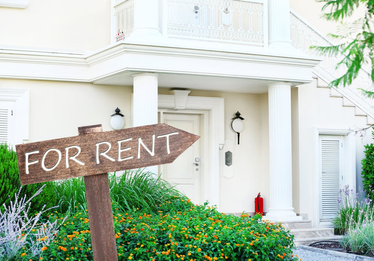 Wooden "For Rent" sign in front of a white house